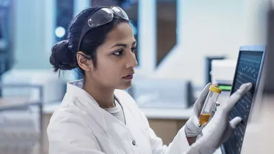 Woman medical scientist looking at a vial and computer screen