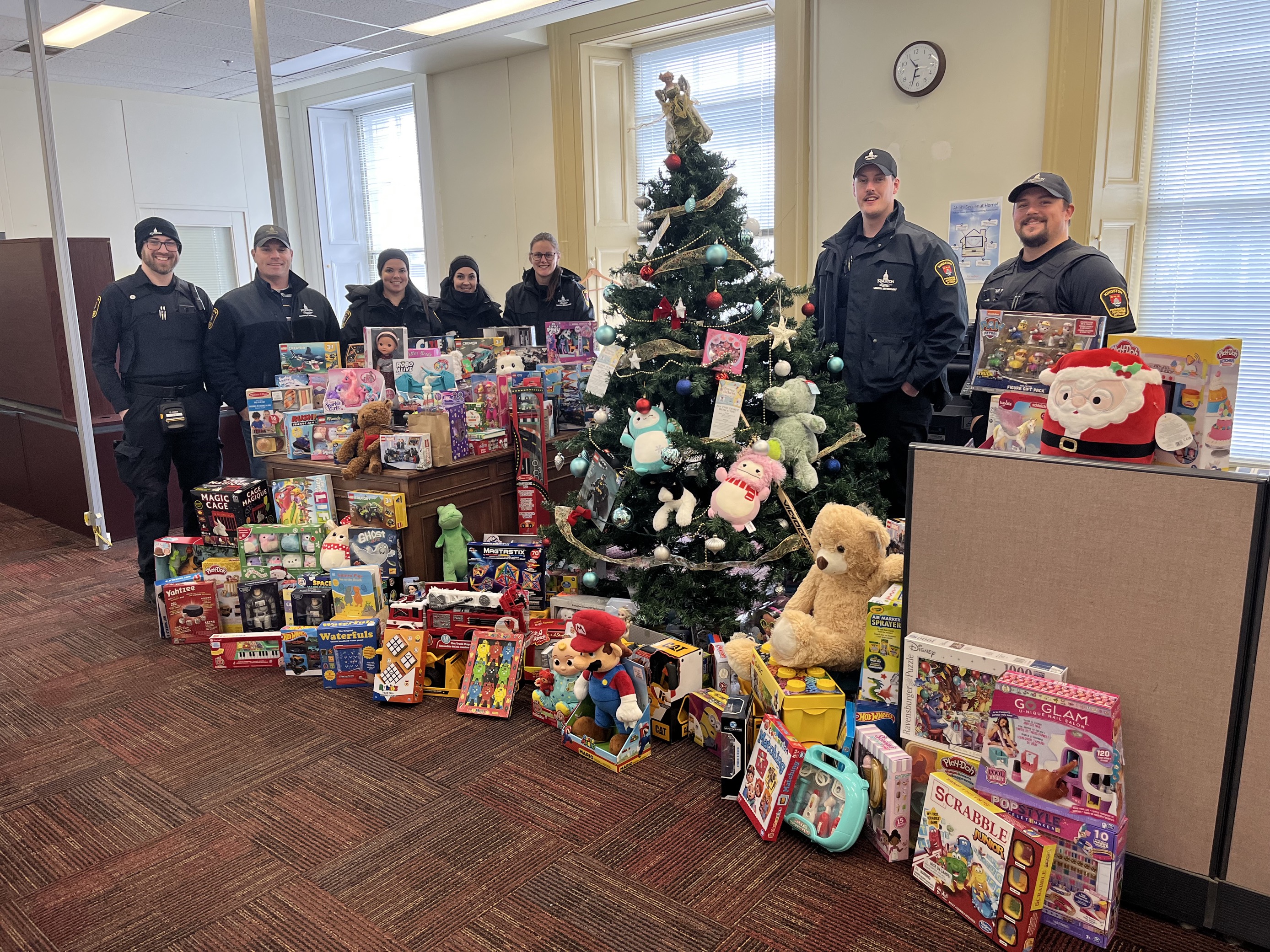 Officers in uniform standing around pile of brand new toys surrounding a Christmas tree.