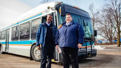 A Kingston transit bus outside with two drivers standing in front of it