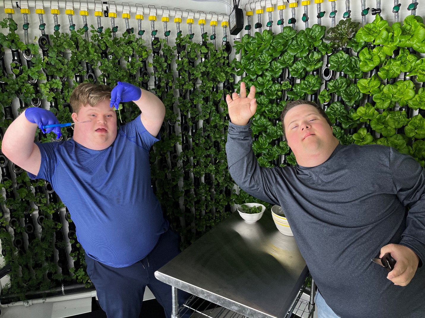 Two participants harvesting produce from a hydroponic greenhouse posing for camera