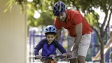 Father helping son learn to ride with bike helmets on