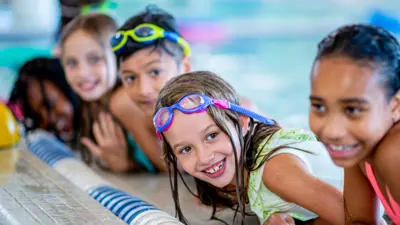 Five kids swimming and leaning on the edge of a pool.