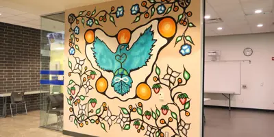 A mural painted on a wall with a blue eagle in the centre along with symbols of the Earth, the Indigenous infinity symbol, flowers, vines and strawberries.