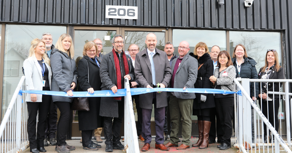 Mayor Bryan Paterson, Councillor Cinanni, City staff and representatives from Addictions and Mental Health Services (AMHS) and Cupido Construction gathered outside the doors of 206 Concession St. standing behind a blue "City of Kingston" ribbon.