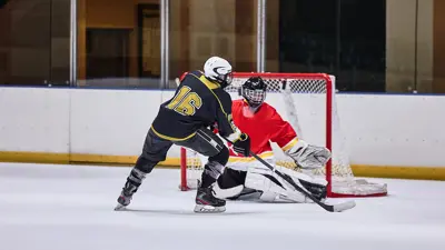 An ice hockey player shooting a puck at a goalie in net on an indoor rink