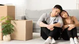 An unhappy young couple sitting inside a home with packing boxes