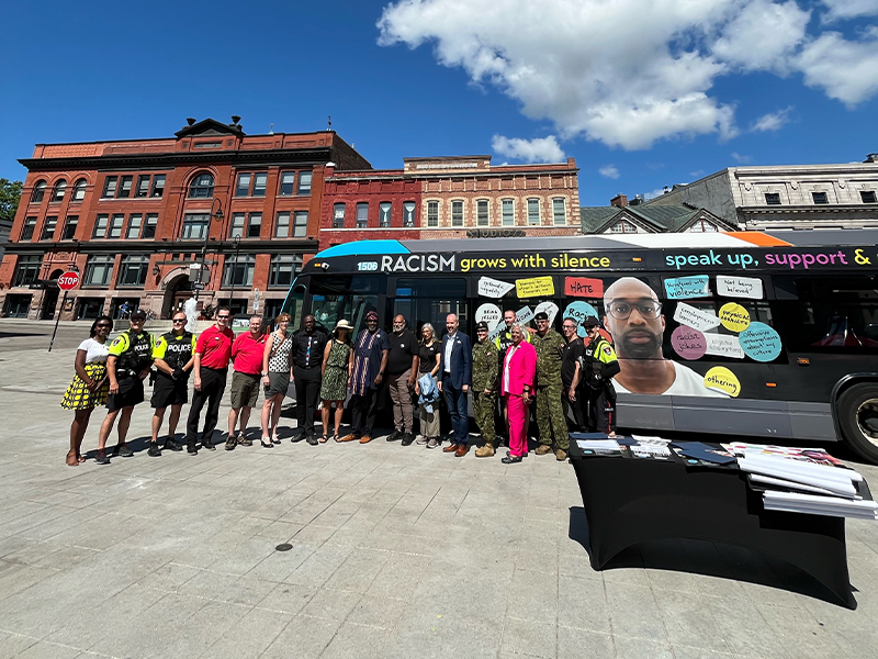 Group of people standing in front of Kingston Transit but with Anti-Racist campaign wrap.