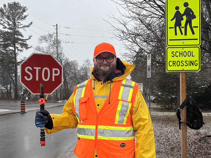 Clayton Ross holding a stop sign standing in front of a school crossing on a snowy morning