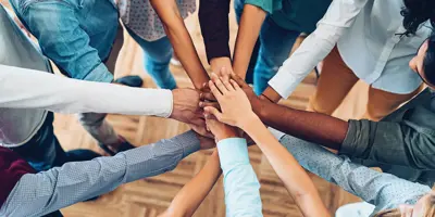 Many different people from different background all reaching out and placing their hands in the centre