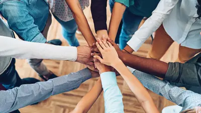 Many different people from different background all reaching out and placing their hands in the centre