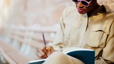 A woman sitting on a bench writing in a book