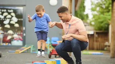 Teacher helping toddler play outside