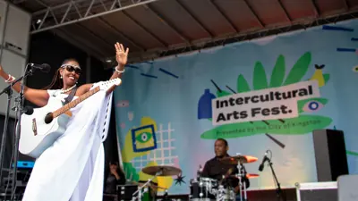 Woman performer with guitar on stage performing at the Intercultural Arts Fest