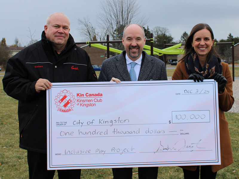 Three people holding a large cheque of one hundred thousand dollars for the City of Kingston.