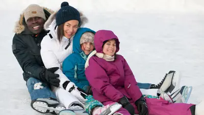 A man and woman with their two children sitting on the ice with ice skates on