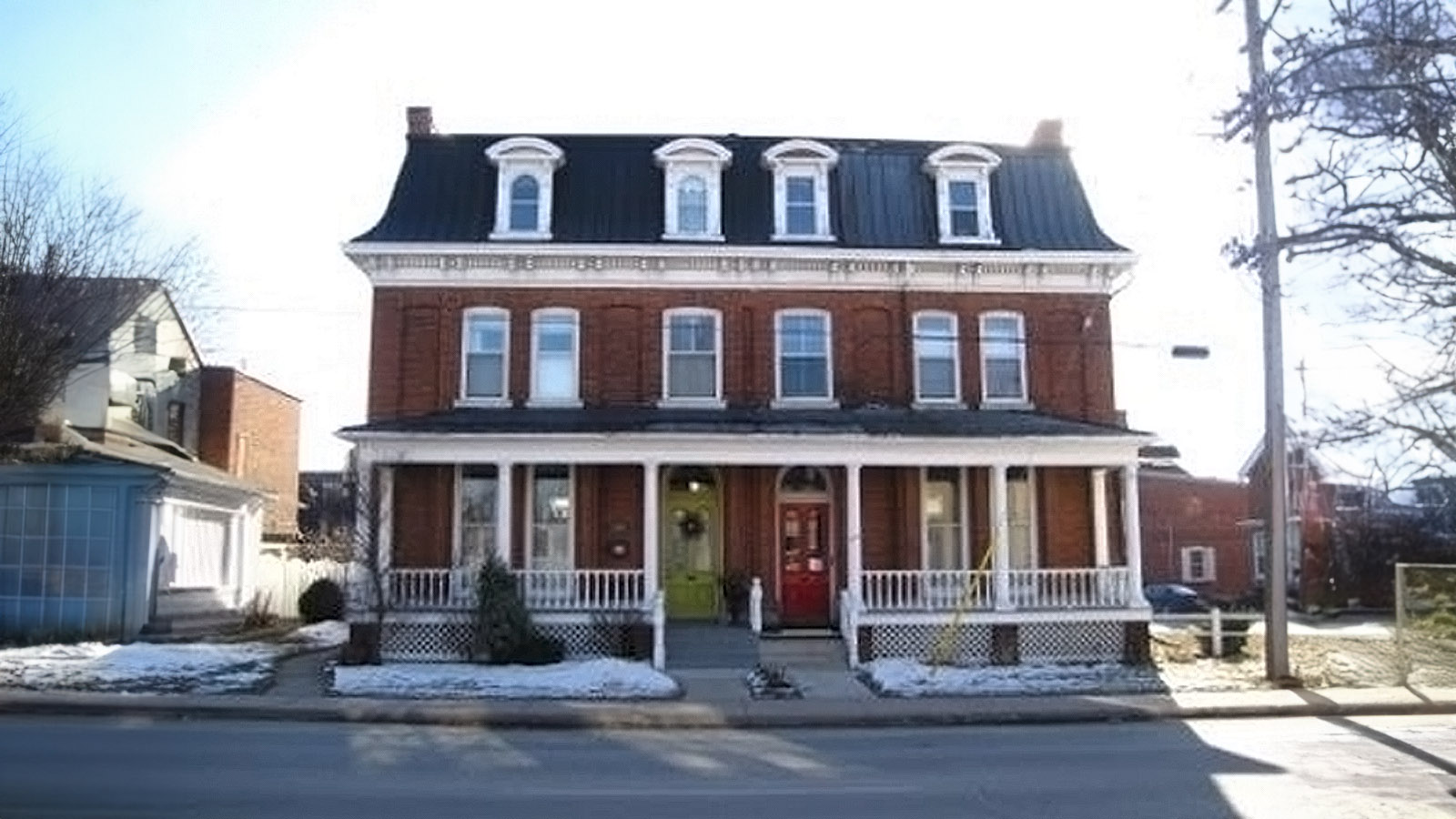 Large historic brick house with a black roof and a front porch.