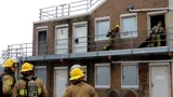 The fire training facility being used by two firefighters on the second floor outside, while three firefighters watch